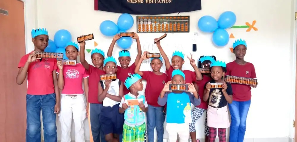 Shenmo Education Rwanda — Student celebration: learners displaying abacuses beneath the Shenmo Education banner.